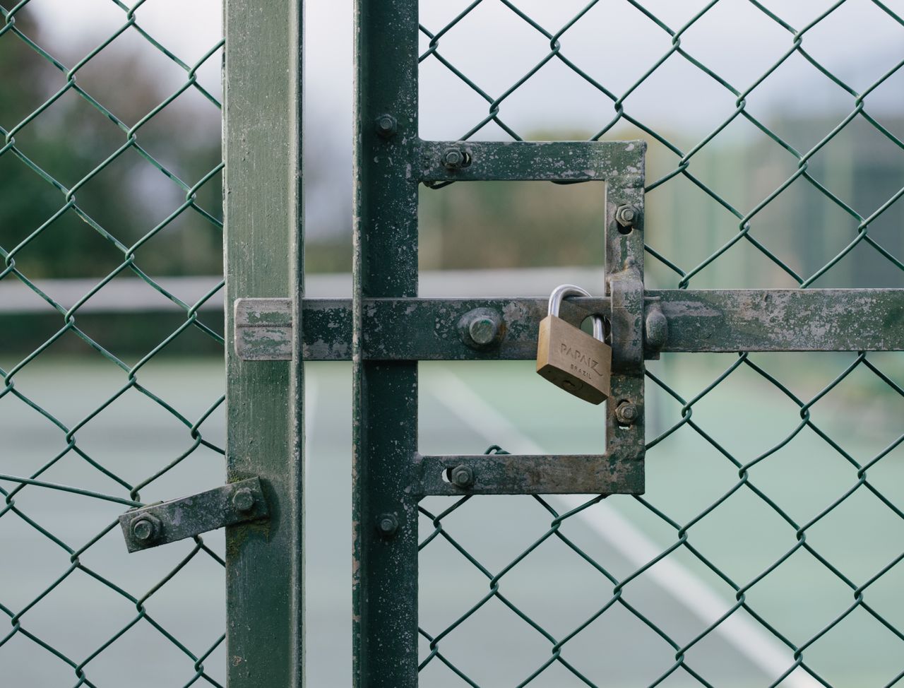 Close-up of a locked gate with chain link fence at a tennis court outdoors.