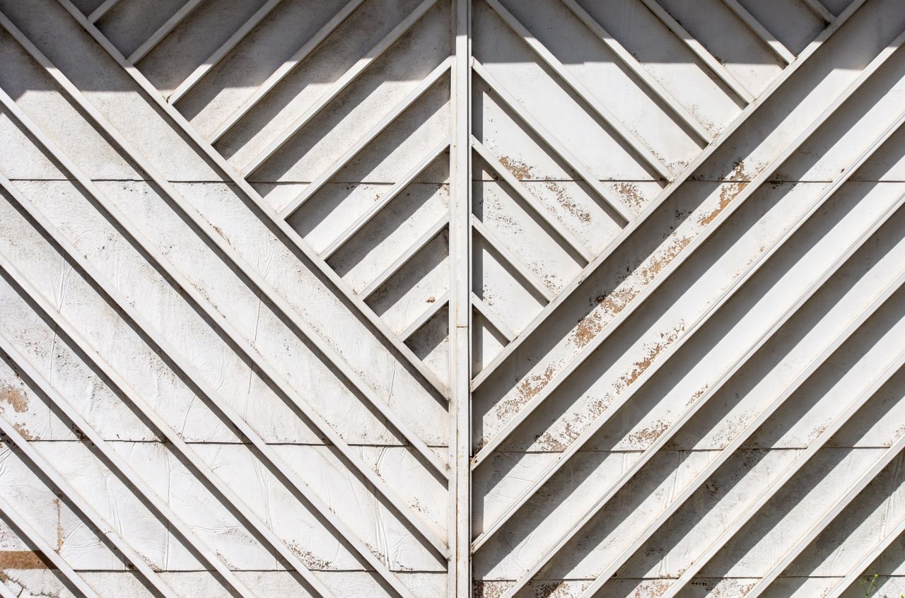Close-up view of a weathered metal gate with geometric patterns and diagonal lines.